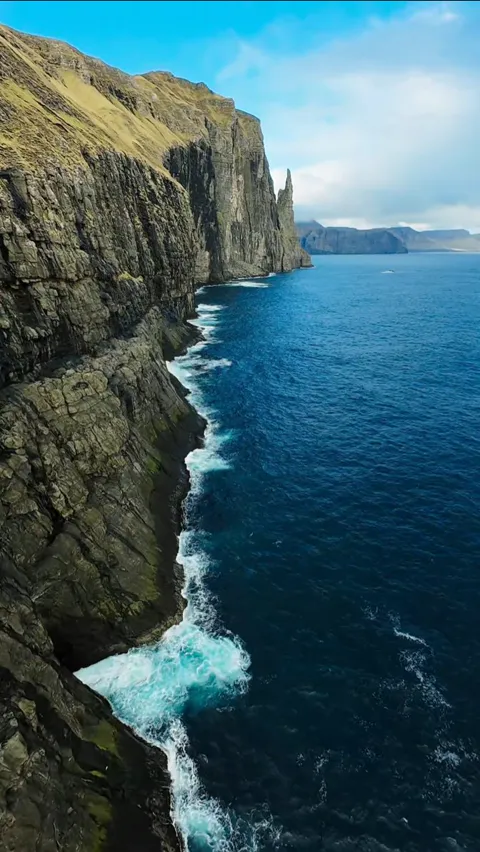 Sunlit layered sea cliffs dropping straight into deep blue ocean, Faroe Islands
