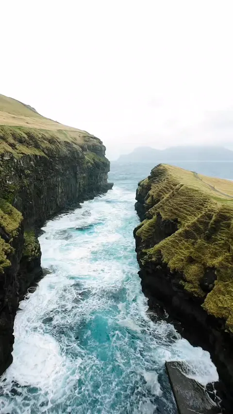 Aerial view of surf pushing through a narrow sea gorge between green cliffs, Faroe Islands