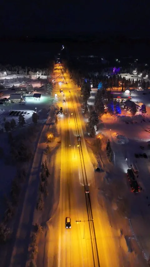 Aerial view of a lit road running through a snowy resort village at night, Lapland, Finland