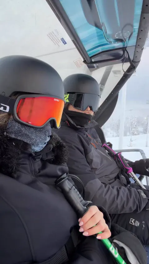 Two skiers in helmets and goggles riding a lift above the snow, Ruka, Lapland, Finland