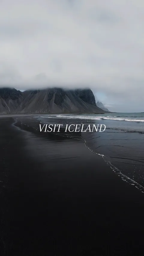 A black sand beach meeting a steep dark mountain under low cloud, Iceland