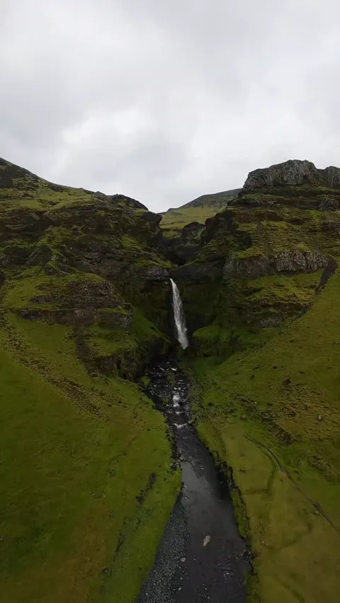 Aerial view of a waterfall dropping into a mossy green canyon, Iceland