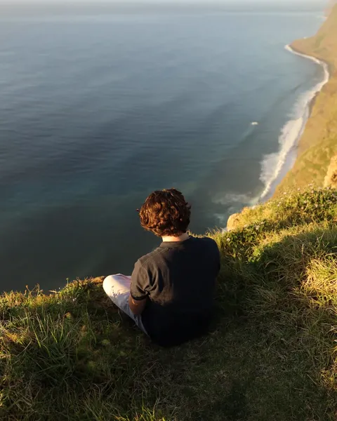 Kristi Leka sitting on a grassy clifftop above the open sea, Madeira
