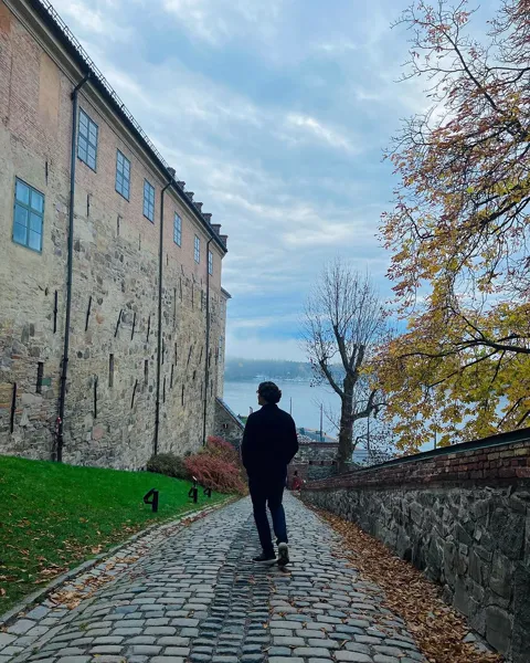 Kristi Leka walking a cobbled path beside a fortress wall in autumn