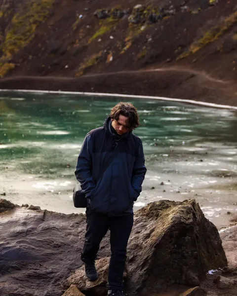 Kristi Leka standing on the shore of a turquoise glacial lake below bare mountains