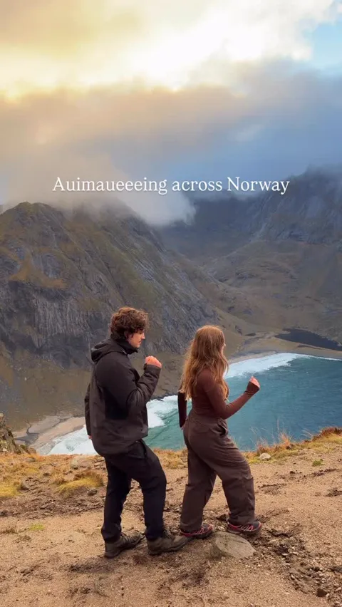 Two people on a clifftop looking down at a turquoise beach far below, Lofoten, Norway