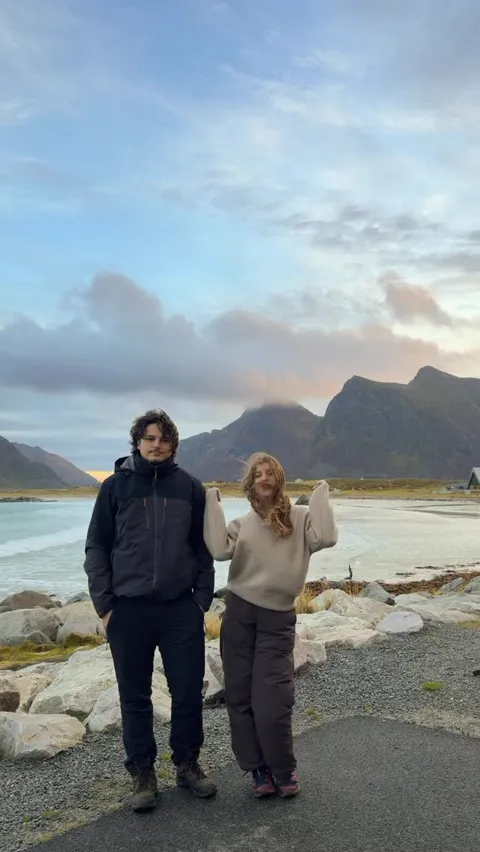 Kristi Leka standing on the road beside a wide Lofoten beach at dusk, mountains behind, Norway