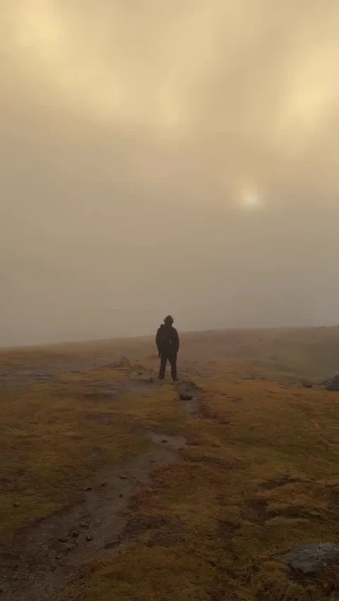 A lone figure standing on a ridge in golden fog with the sun breaking through, Lofoten, Norway