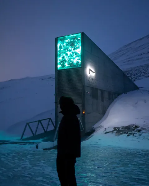 The illuminated entrance of the Svalbard Global Seed Vault glowing turquoise against the snow