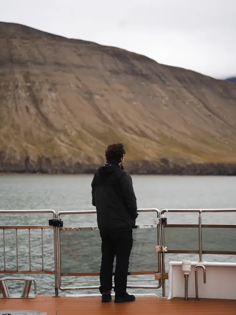 A person at a ship's railing looking out at an Arctic fjord and bare mountainside, Svalbard