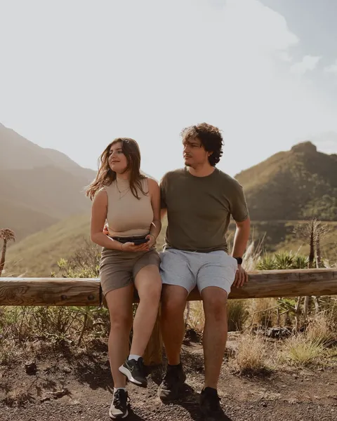 Two people resting on a wooden rail with dry volcanic hills behind, Tenerife